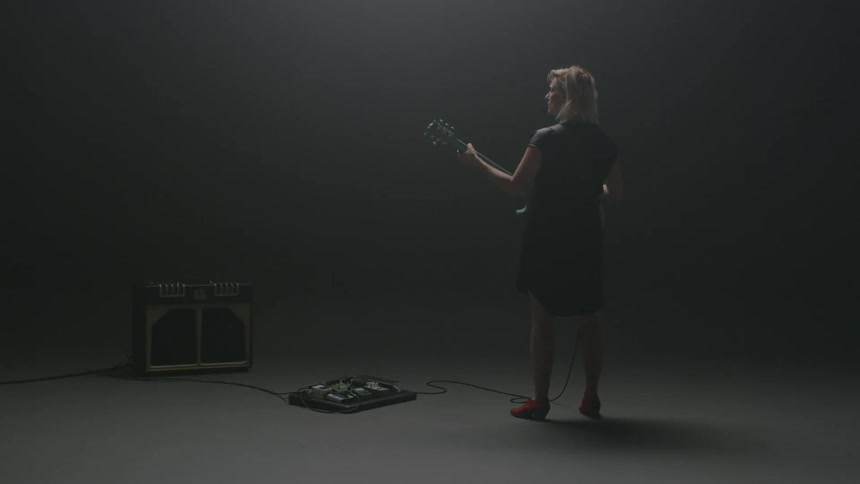 A woman plays guitar in an empty room