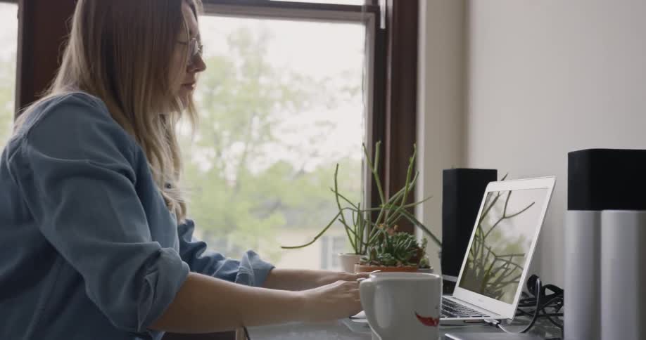 Female Business Owner sits down and opens her laptop before writing in a pad