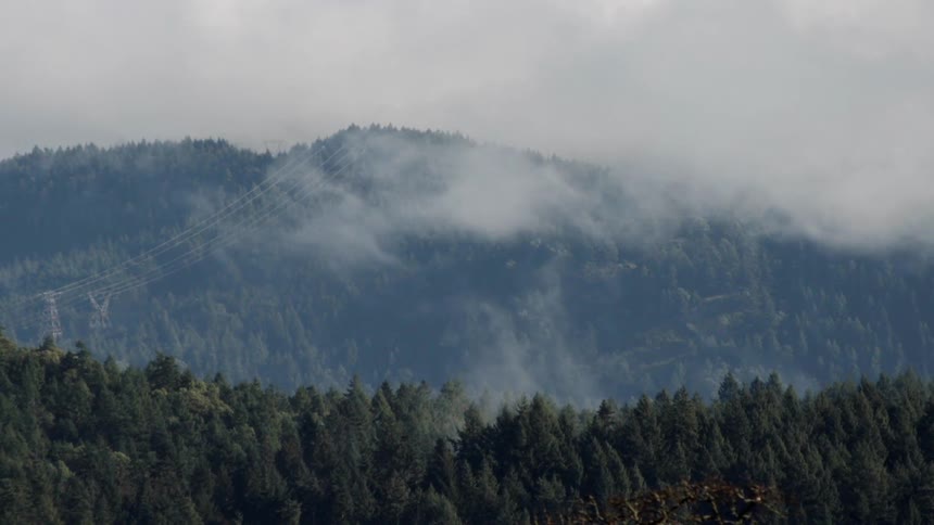 Clouds and haze pass above woods at the foot of a mountain