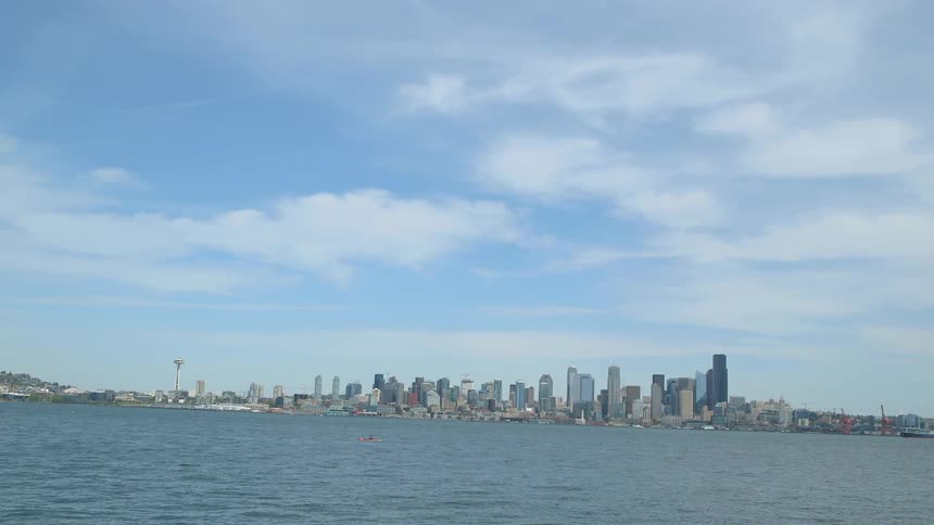 Small watercraft on the waters before a large city in the distance with some clouds in the sky
