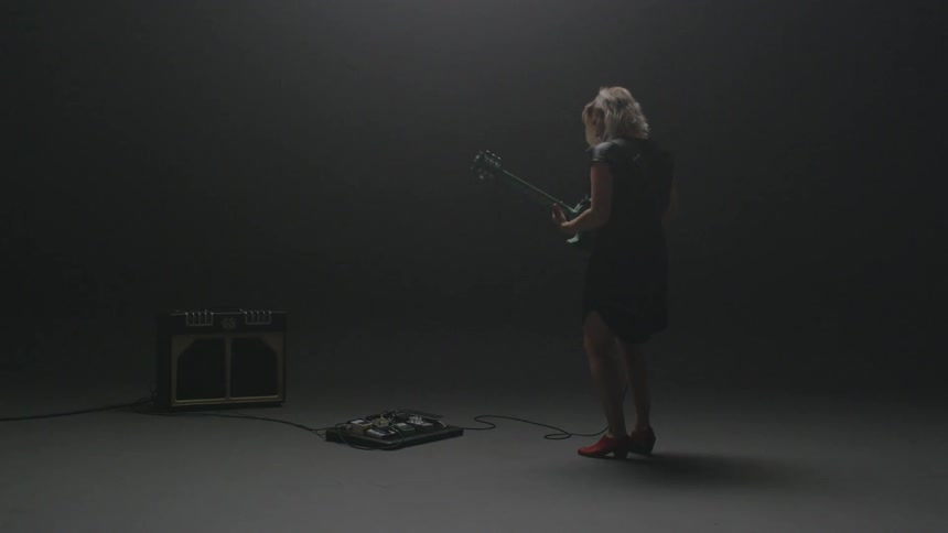 A woman plays guitar in a dim room