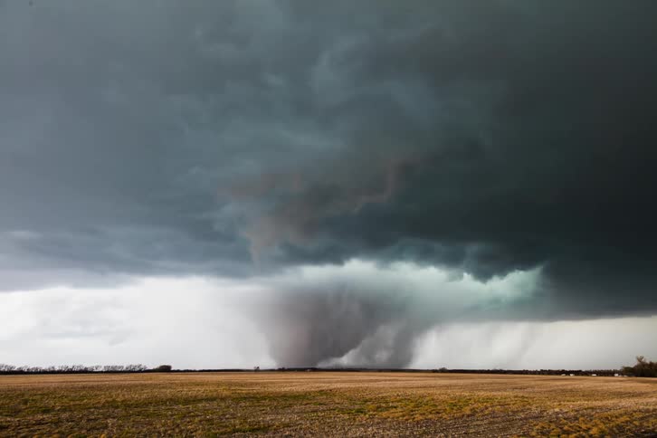 The tornado forms and moves over the field in the distance