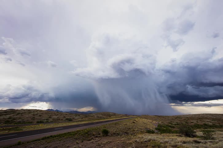 Cars drive down the road towards the storm forming ahead