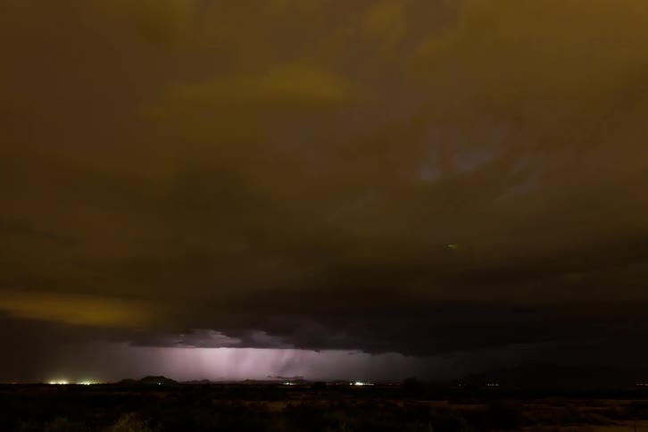 A lightning storm is moving over a desert community at night