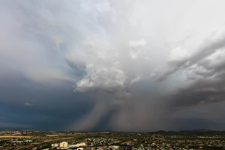 Storm clouds are dropping rain over a valley during the day
