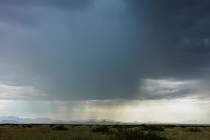 A storm is dropping rain over a desert setting in daylight