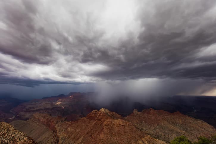 Storm clouds pass above a large canyon as rain falls