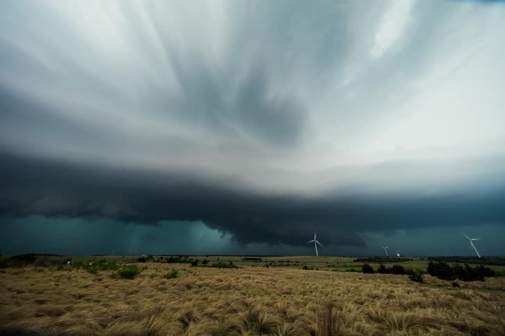 A storm brews over an open grass field with windmills rotating