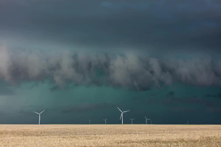 A storm is blowing across a wind turbine farm at dusk