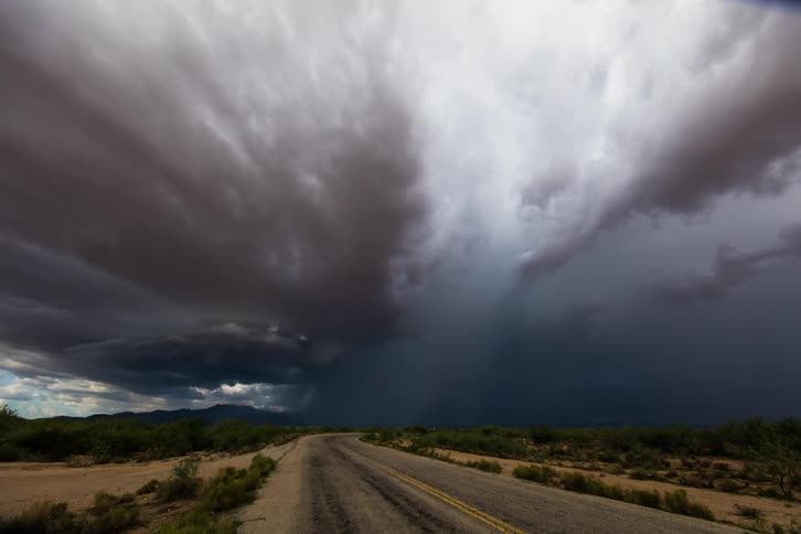 Cars drive on the road as the storm chases behind