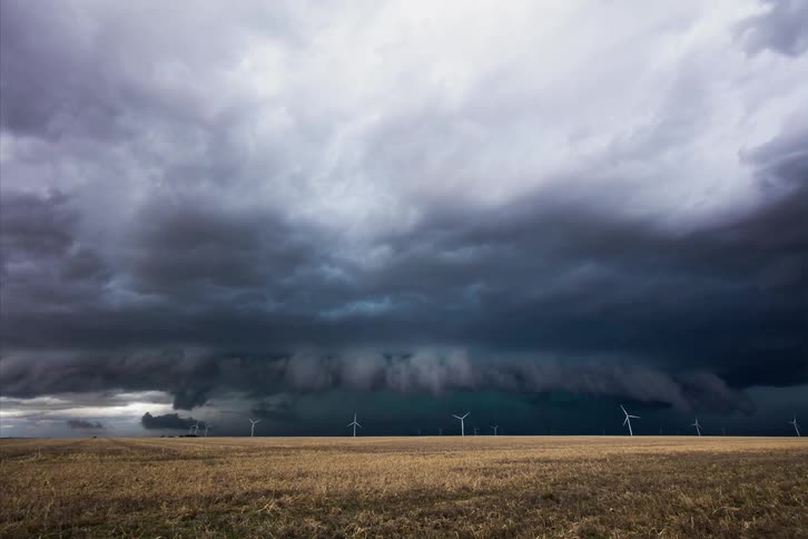 A storm is blowing across a wind turbine farm at dusk