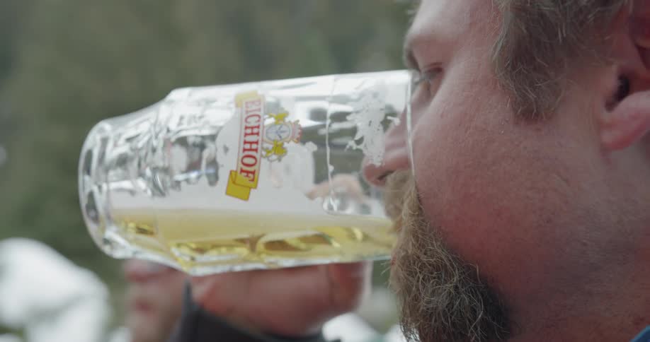 A man with mustache finishes his beer from a glass mug