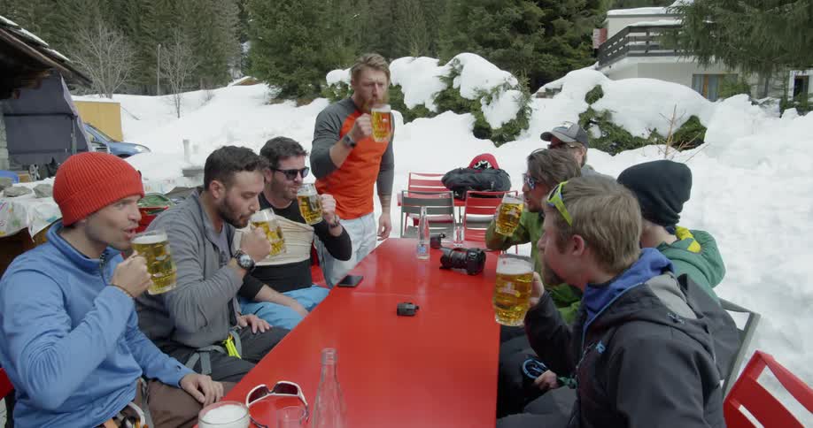 A group of men clank glasses and drink beer out in the snow