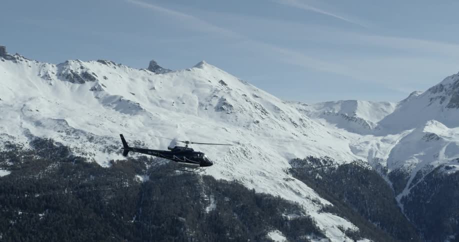 Helicopter flying near snowy mountains on a somewhat cloudy day