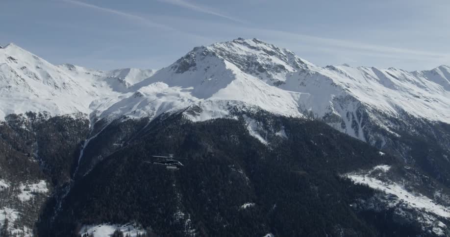 A helicopter is piloted over snowy mountains