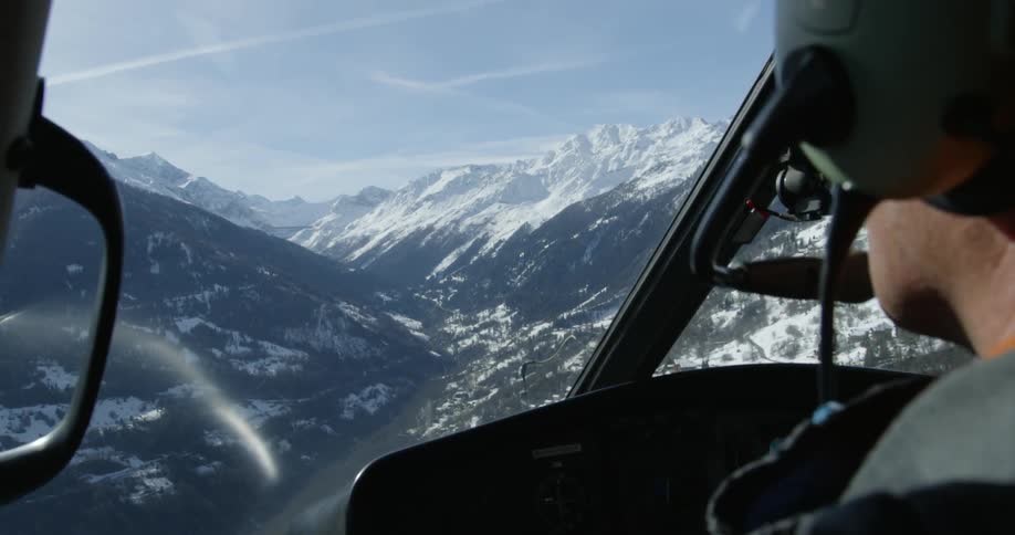 Helicopter flying near snowy mountains on a somewhat cloudy day