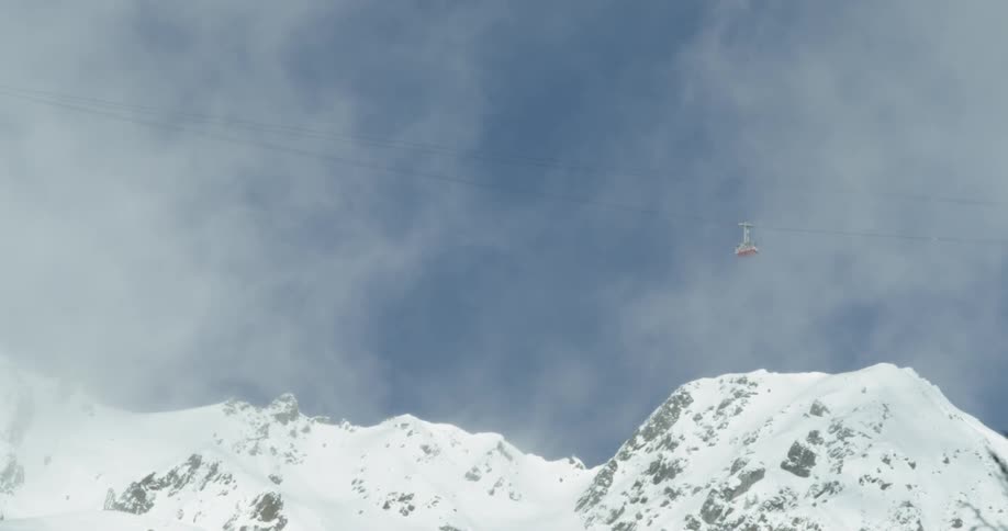 Ski lift passing near some snowy mountains on a cloudy day