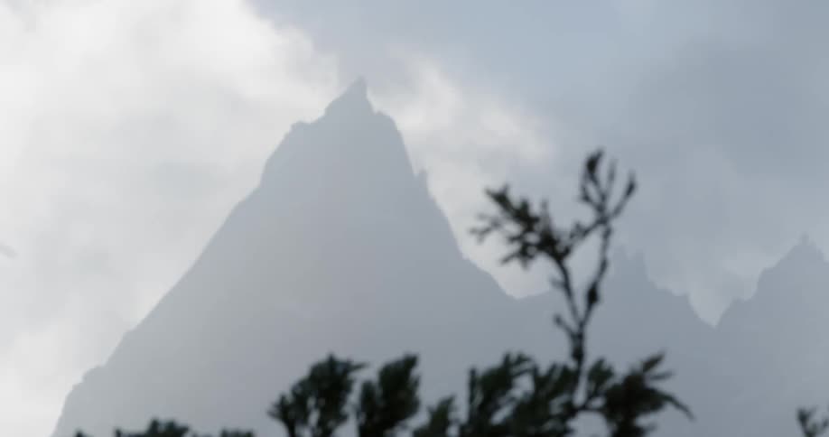 Clouds pass above a tall mountain on a hazy day