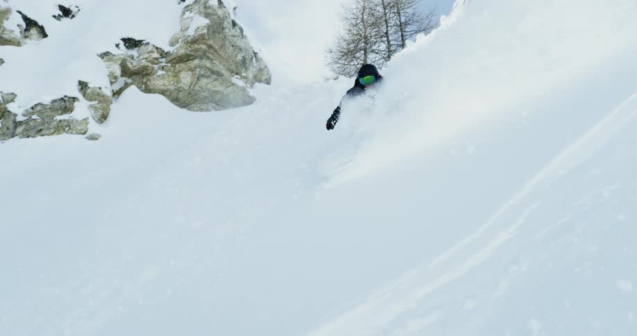 Snowboarder riding the deep snow down a hill on a cloudy day