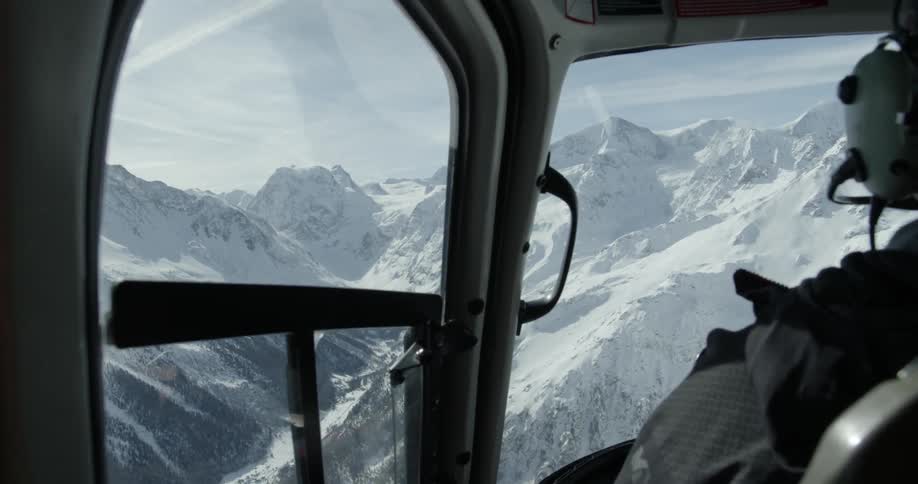 A helicopter is piloted over snowy mountains