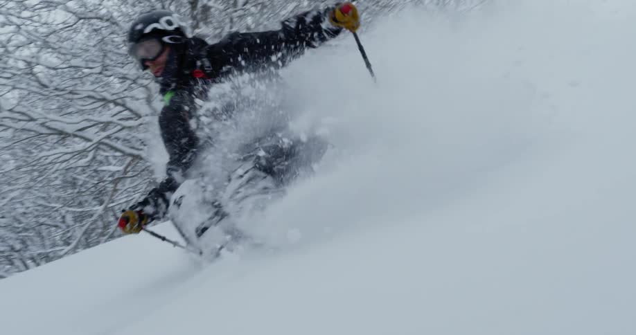 A skier jumps off a hill onto a slope of fresh powder