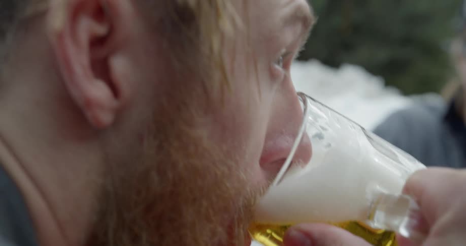 A bearded man takes a drink of beer