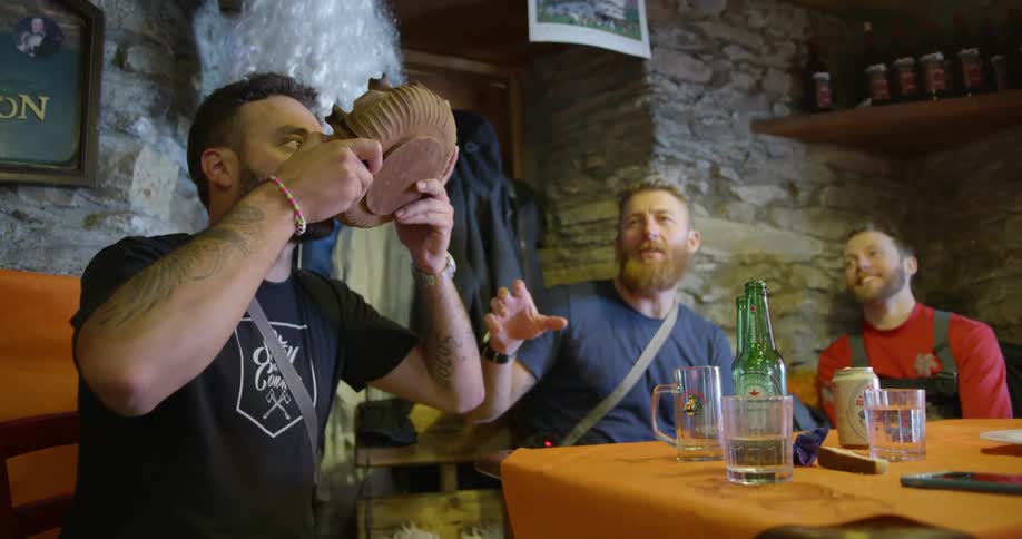 Bearded men sitting around a pub table as one of them drinks from a bowl