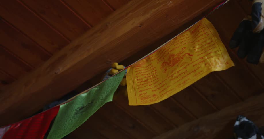 Prayer flags are hanging from the ceiling beam in old wooden hut