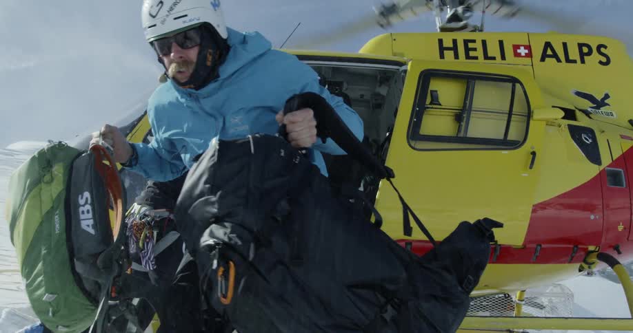 A man is hauling bags as he unloads from a helicopter on a mountainside during the day