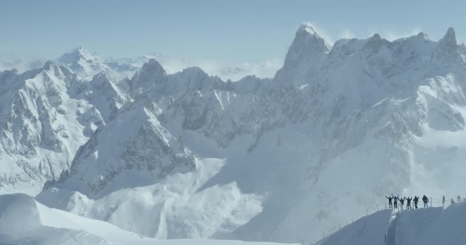 A group of people are standing on a mountain ledge looking at a mountain range in winter