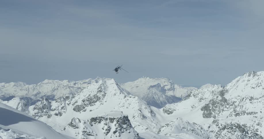 A helicopter turns and flies over snow covered peaks