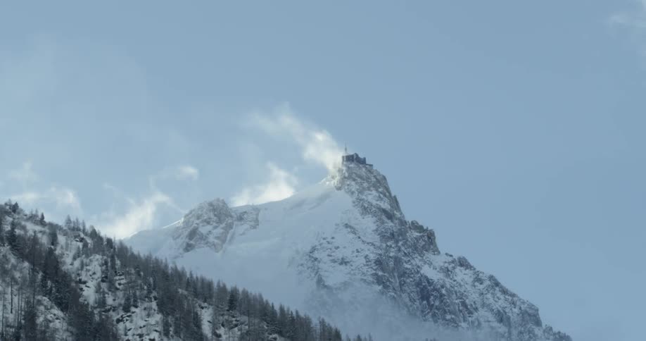 Snow is drifted off the top of a mountain