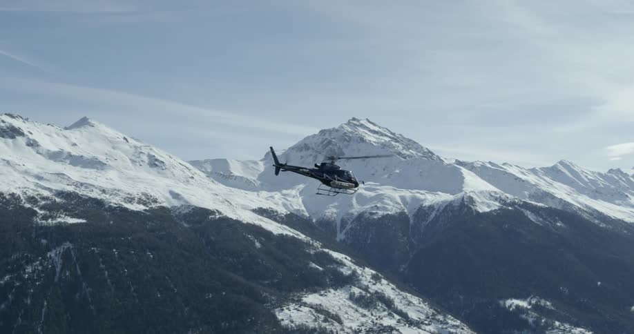 A helicopter is piloted over snowy mountains