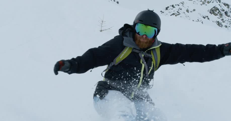 A man is snowboarding down a mountain during the day