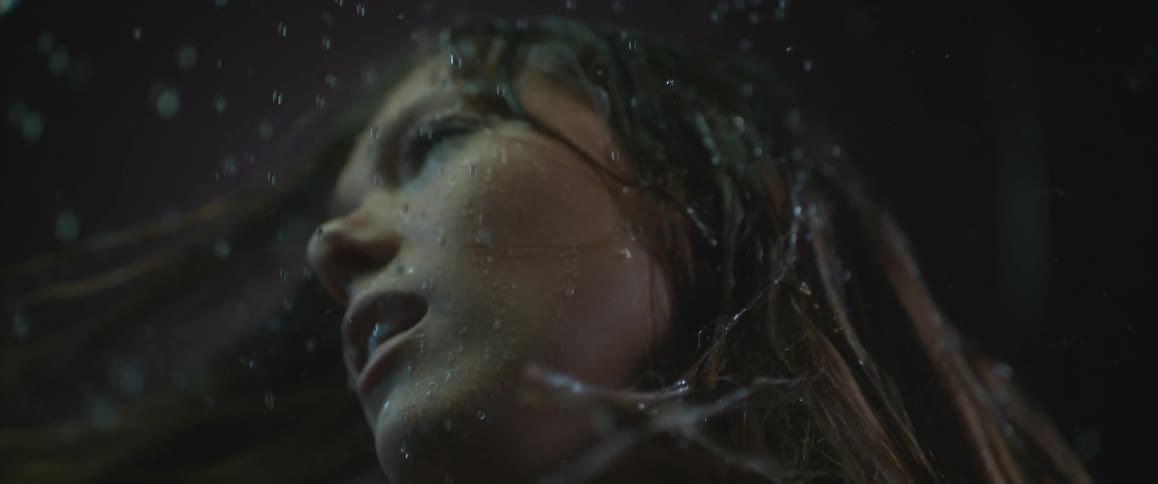 Slow motion shot of water falling on a blonde woman's hair as she whips her head around
