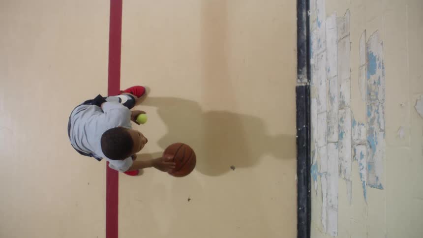 A boy dribbles a basketball while tossing and catching a tennis ball