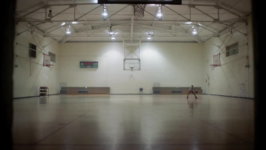 Person dribbling two basketballs at the same time in a large gymnasium