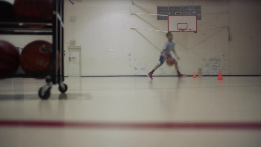 A boy is practicing his basketball dribbling skills inside during the day