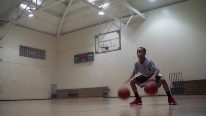 A boy is practicing his basketball dribbling skills inside during the day