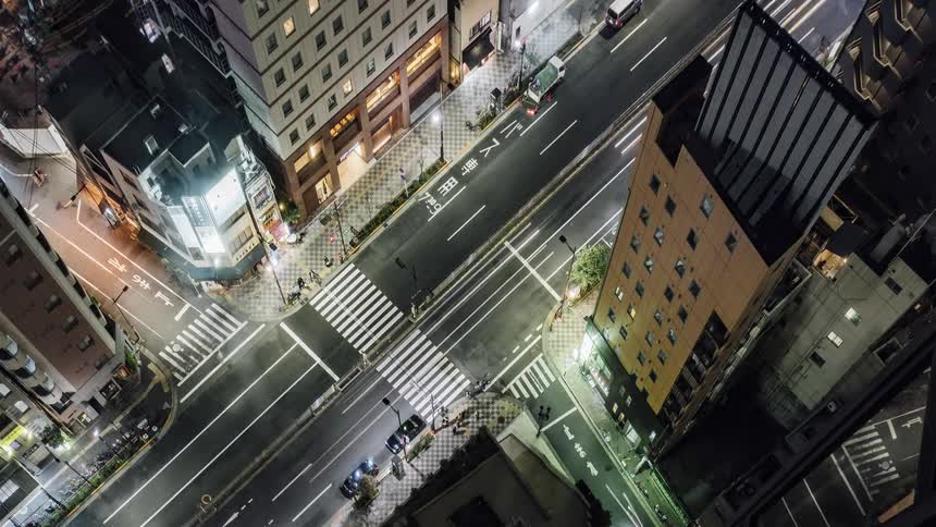 Traffic and pedestrians travel along a street in an urban area at night