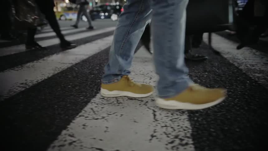 People's legs and feet as the walk on a busy sidewalk at night