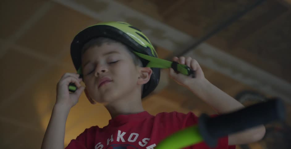 A child reaches and picks up his helmet before buckling it