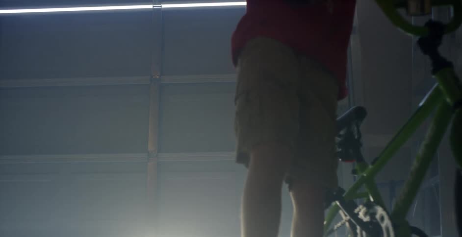A young boy pushes a green bicycle in a garage