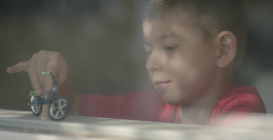A boy plays with a toy bicycle on a window sill