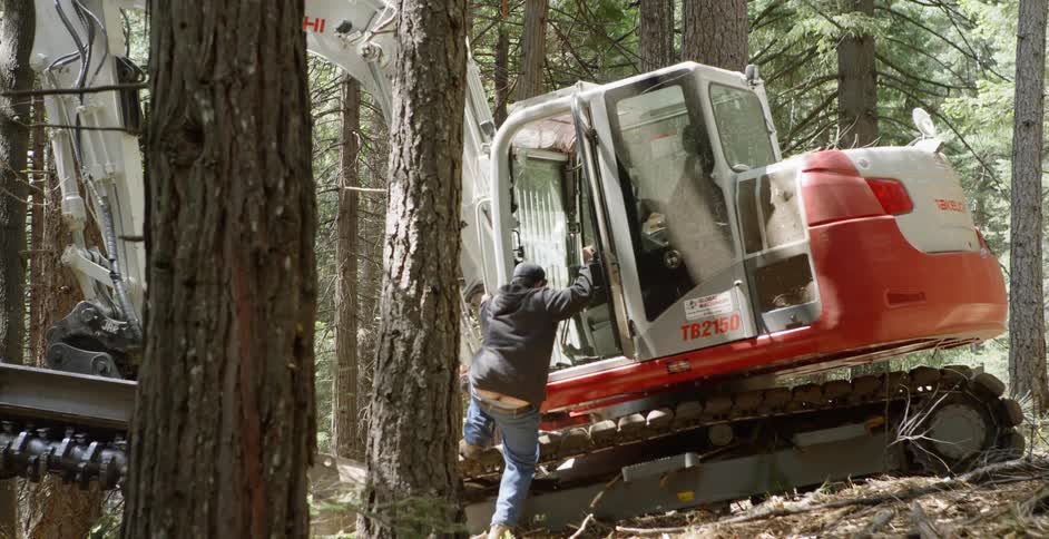 Man entering a piece of heavy equipment machinery in a wooded area