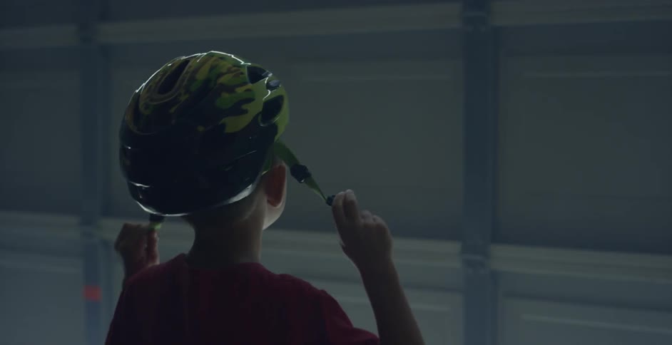 Young boy putting on a bicycle helmet after removing it from the handlebar of his bike in a garage