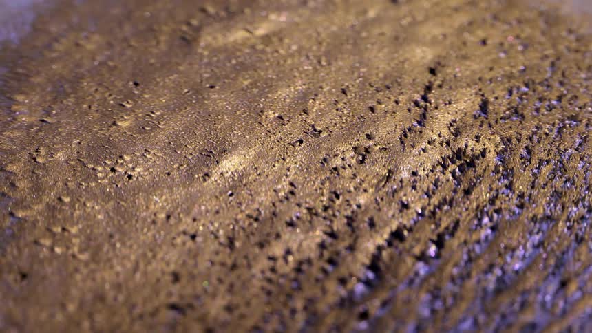 A golden metallic sand moves in a magnetic pattern