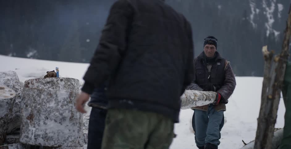 Men carry a long log over the snow covered field