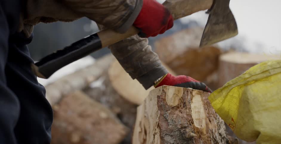 A man uses an ax to cut the bark off a log