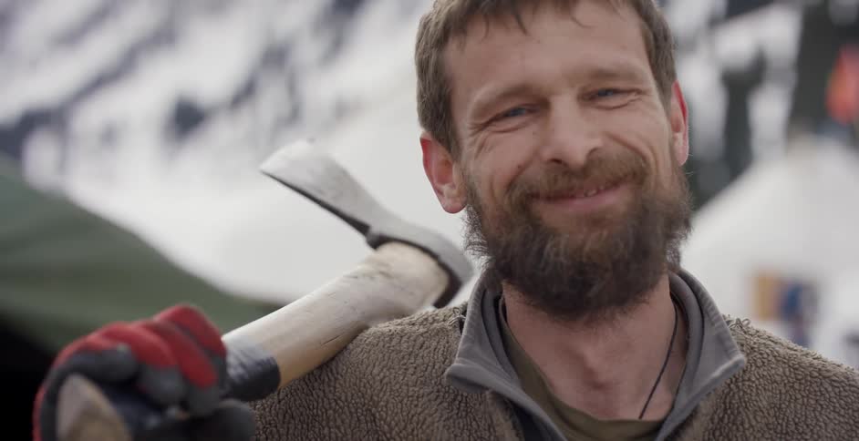 Man smiles as he holds an ax on his shoulder